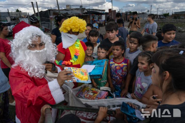 14일(현지시간) 아르헨티나 부에노스아이레스에서 한 무료 급식단체가 주최한 크리스마스 사전 축하 행사가 열려 산타 복장을 한 남성이 빈민가 아이들에게 선물을 나눠주고 있다. 2024.12.15. (출처: 뉴시스)