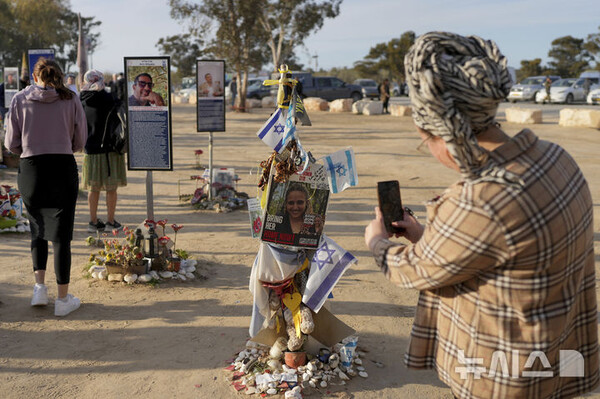19일(현지시간) 가자지구 국경 근처 남부 이스라엘 노바 음악 축제 현장에 마련된 추모 공간에서 하마스에 의해 살해되거나 납치된 희생자들을 기리기 위해 세워진 기념비들 중 하나인 로미 고넨의 사진과 메시지를 한 여성이 촬영하고 있다. (출처: 뉴시스)