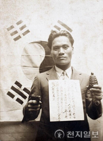 윤봉길 의사가 선서문과 권총, 폭탄을 양손에 들고 태극기 앞에서 기념촬영을 하고 있다. (제공: 윤봉길의사기념사업회) ⓒ천지일보DB
