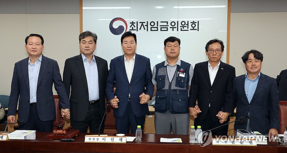 10일 정부세종청사에서 열린 제12차 전원회의에서 내년 최저임금을 시간당 1만320원으로 17년만에 합의로 결정한 공익위원-사용자위원-근로자위원들이 손을 잡고 기념촬영을 하고 있다. 왼쪽부터 하헌제 상임위원, 이인재 위원장, 사용자위원인 류기정 한국경영자총협회 전무, 근로자위원인 류기섭 한국노총 사무총장, 사용자위원인 이명로 중소기업중앙회 인력정책본부장, 공익위원인 권순원 숙명여대 교수. (출처: 연합뉴스)