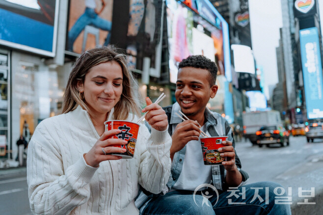 미국 뉴욕 타임스퀘어에서 현지 소비자들이 농심 신라면을 즐기고 있다. 미국 내 현지 생산 기반을 갖춘 농심은 관세 여파를 일부 회피하고 있지만, 소비 둔화에 따른 실적 압박은 여전하다. (제공: 농심)