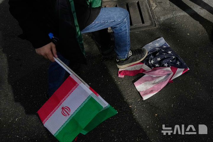 A school boy stomps a U.S. flag as he holds an Iranian flag during an annual rally in front of the former U.S. Embassy in Tehran, celebrating the anniversary of the 1979 takeover of the embassy, Iran, Tuesday, Nov. 4, 2025. (AP Photo/Vahid Salemi, 뉴시스)